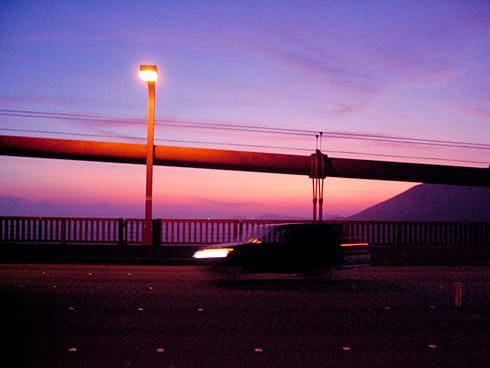 Sun setting behind bridge cables with traffic blurring by Sun setting behind bridge cables with traffic blurring by
