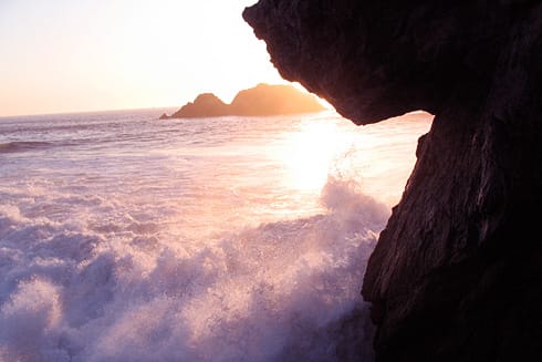 Sunset behind wave crashing onto beach rocks Sunset behind wave crashing onto beach rocks
