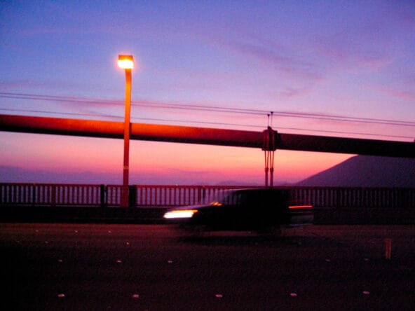 Sun setting behind bridge cables n traffic blurring by